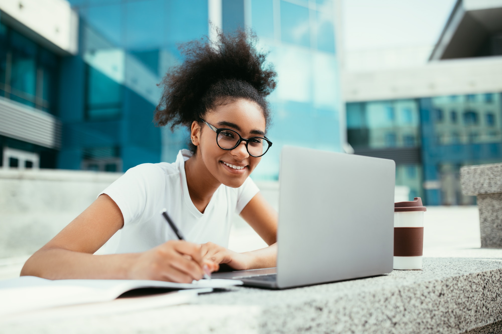 Cheerful African Student Girl Taking Notes At Laptop Outdoor